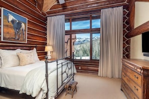 A log cabin bedroom with a bed, a dresser, a window with curtains, and a painting of a horse.