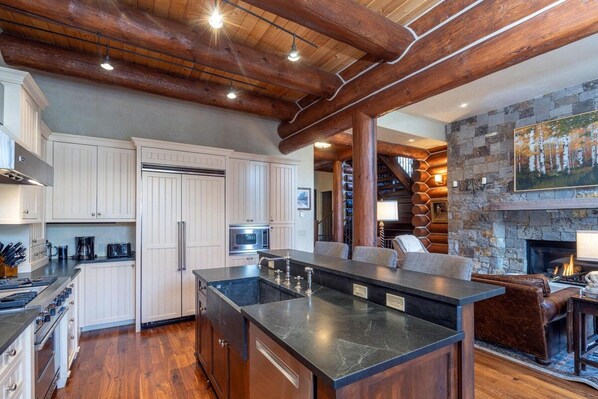 A modern kitchen with a central island, white cabinetry, and a stone fireplace.
