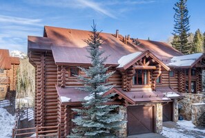 Une cabane en rondins, avec des fondations en pierre, un toit en métal et un paysage enneigé.
