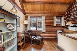 L’intérieur d’une cabane en rondins, avec un fauteuil en cuir, une petite table et une bibliothèque.