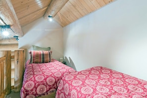 A small, cozy room with a sloped ceiling, a single bed with a patterned bedspread, and a wooden chair.