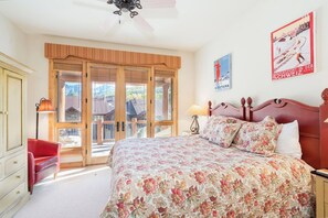 Une chambre avec un grand lit, un fauteuil rouge, une armoire en bois et une vue sur l’extérieur.