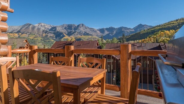 A wooden deck with a table and chairs overlooking a mountainous landscape. - Villas At Tristant 215 (Mountain Village)