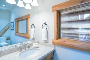 Une salle de bain avec un grand miroir, un cadre de fenêtre en bois et un lavabo équipé de deux robinets.