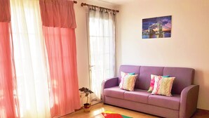 A living room with a purple sofa, colorful cushions, a multicolored rug, and a painting of a bridge.