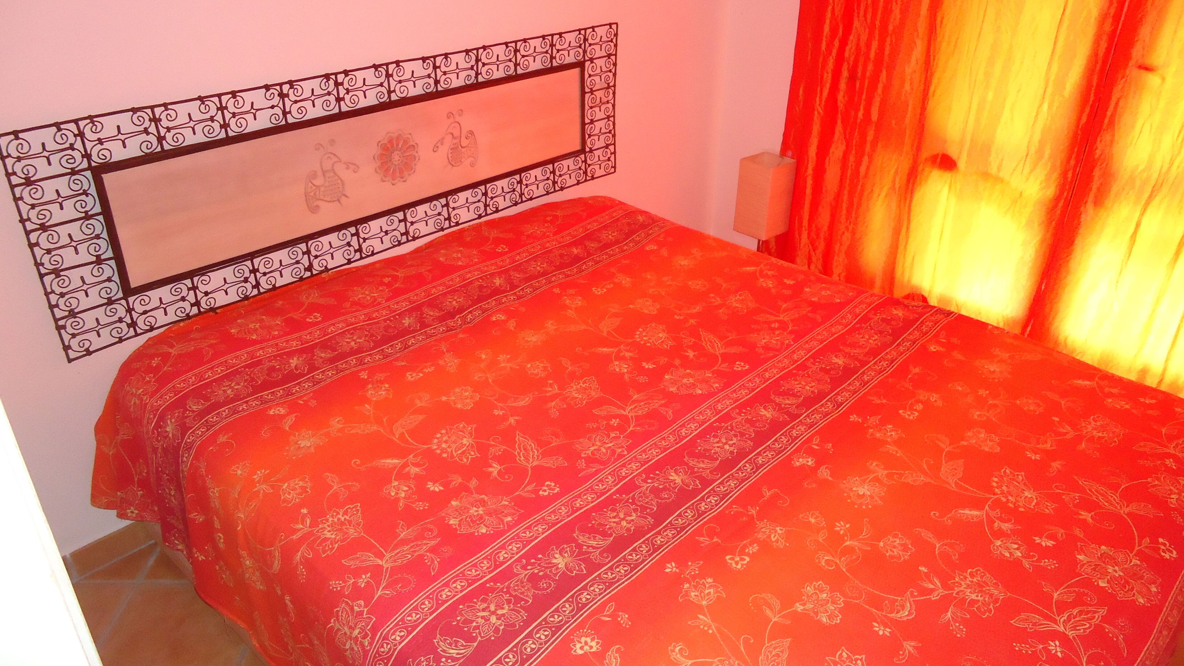 A bed with a red floral bedspread and a decorative headboard with a geometric pattern.