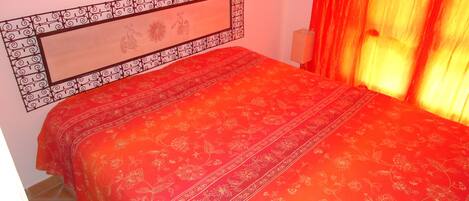 A bed with a red floral bedspread and a decorative headboard with a geometric pattern.