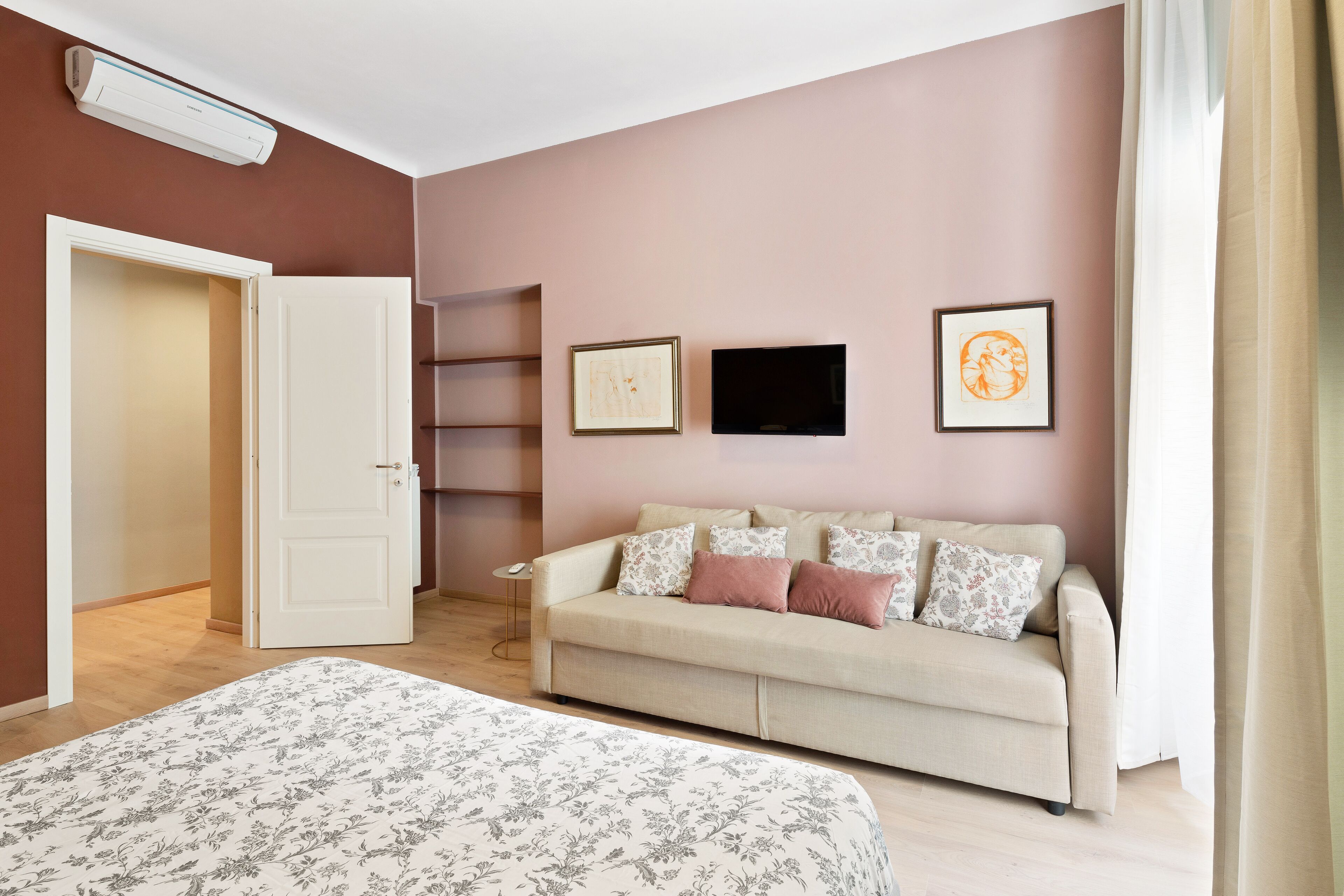A bedroom with a bed, a sofa, a TV, and framed pictures on the wall.