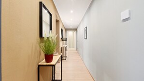 Un pasillo moderno con suelo de madera, una planta en maceta, un espejo e interruptor de luz en la pared.