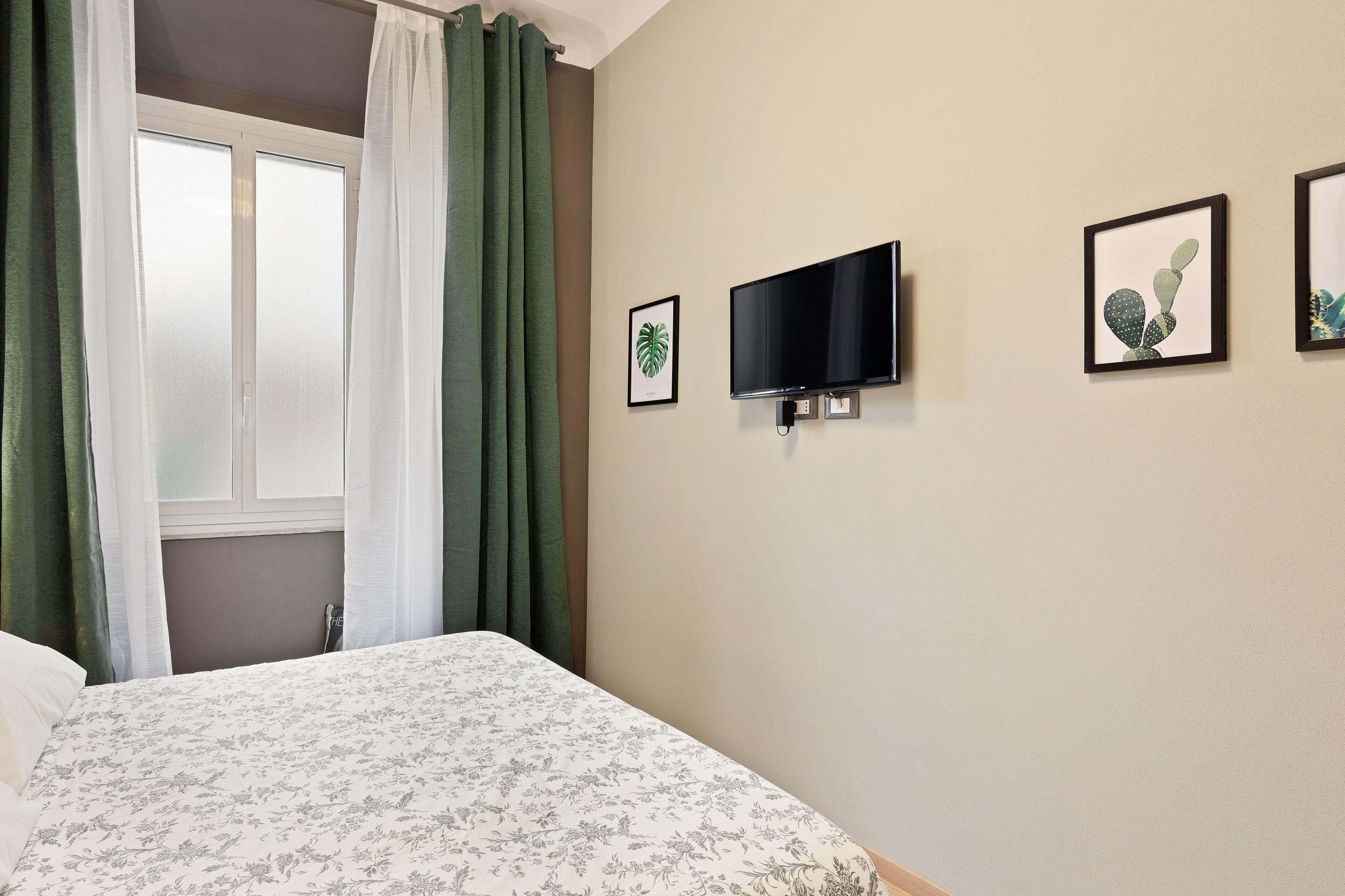 A hotel room with a bed, a TV mounted on the wall, and framed pictures on the wall.