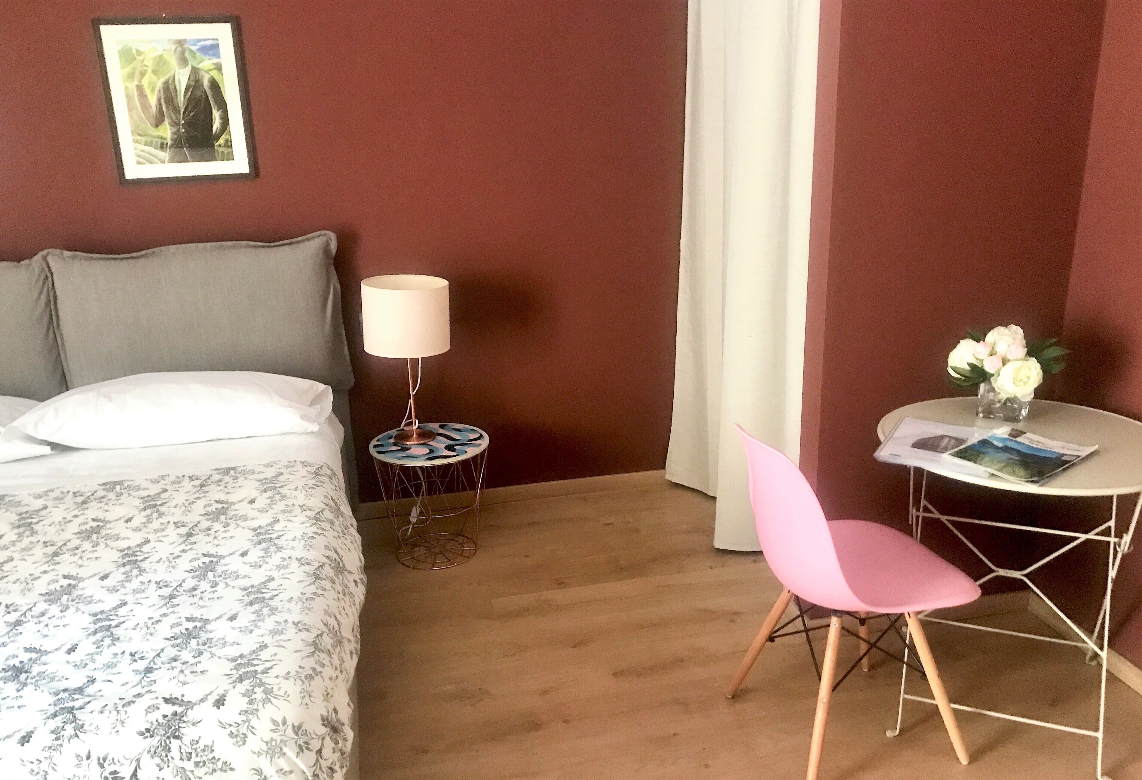A hotel room with a bed, a small round table with a chair, a lamp, and a picture on the wall.