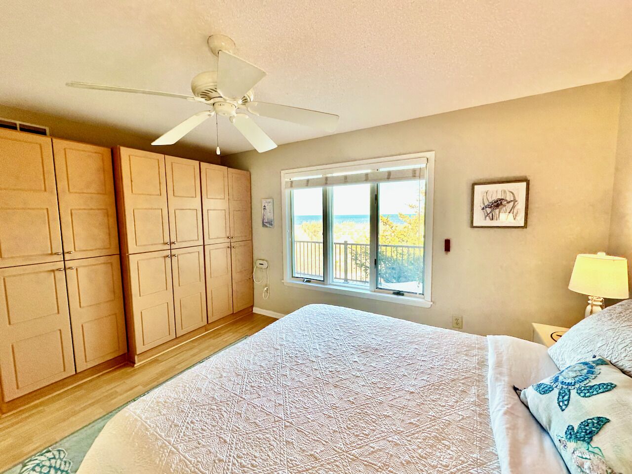 Une chambre à coucher avec un lit, un ventilateur de plafond, une fenêtre donnant sur un beau paysage et des armoires en bois.