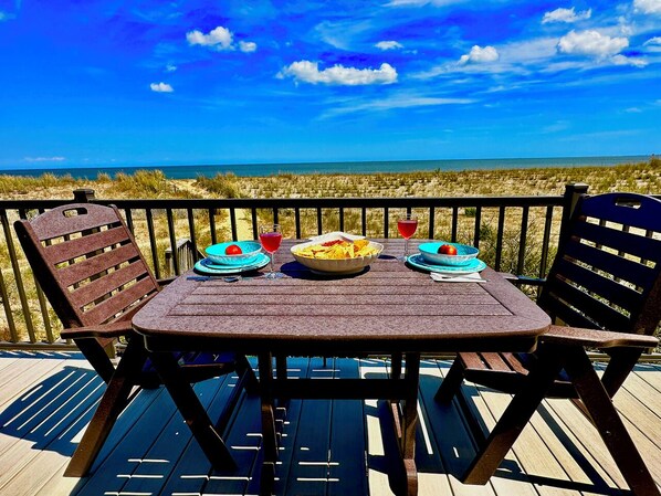 A wooden deck with a table set for two, overlooking a beach.