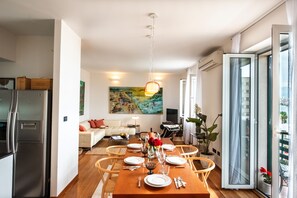 A modern kitchen with a built-in refrigerator, dining area with a wooden table set for four, and a large window with a view of the city.