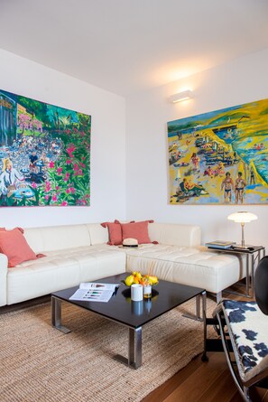 A living room with a white sofa, a coffee table with fruits, and two large paintings on the walls.