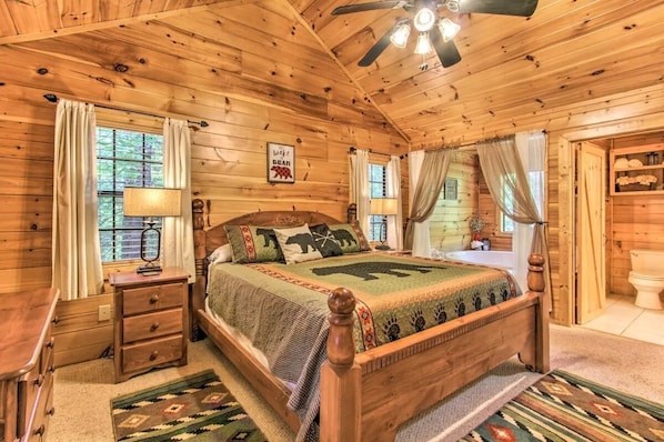 Camera da letto in una baita di legno, con un letto, comodini, una ventola a soffitto e una finestra con tende.