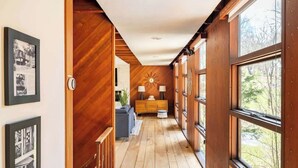 A hallway with wooden walls and large windows, a sofa, and a lamp.