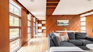 A modern interior with a wooden floor, a dark grey sofa, and a dining area with a white table and chairs.