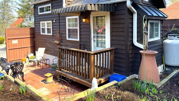 A two-story house with a balcony, a small porch, and a garden area with outdoor furniture.