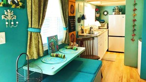 A compact kitchen with a dining area, a small refrigerator, and a window with curtains.