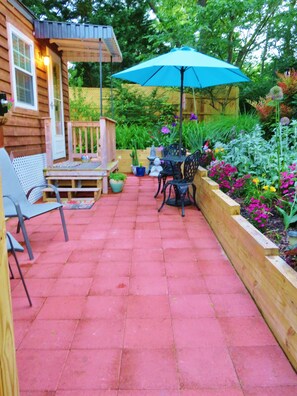 A patio with red tiles, a wooden deck, a table with chairs, and a blue umbrella.