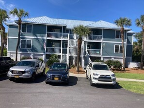 A multi-story building with a blue exterior and white railings. There are three cars parked in front.
