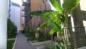 A narrow pathway flanked by lush greenery and modern buildings with balconies. - VICTOR HUGO AP4159 by RIVIERA HOLIDAY HOMES (Niza)