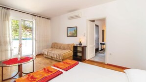 A hotel room with a bed, a table with a glass top, a sofa, a painting on the wall, and an air conditioning unit. - Stunning home in Bakarac with house sea view (Bakarac)