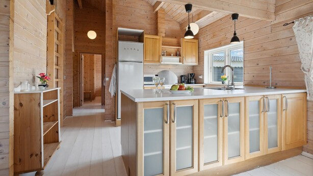 A wooden cabin interior with a kitchen featuring a central island, wooden cabinets, and pendant lighting.
