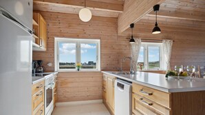 A modern kitchen with wooden walls, a large window, and a view of the countryside.