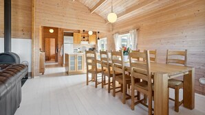 A wooden cabin interior with a dining area, kitchen, and a fireplace.