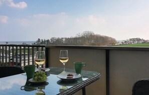 A balcony with a table set for two, featuring a glass of white wine, a green cup, a plate with grapes, and a plate with pastries. - Beach front apartment in Heringsdorf-Süssau (Heringsdorf-Süssau)