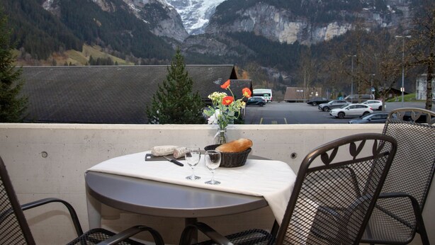 A table with a vase of flowers, a bottle, and a basket of bread, overlooking a parking area and mountains. - Chalet Abendrot apARTments by Interhome (Grindelwald)
