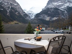 A table with a vase of flowers, a bottle, and a basket of bread, overlooking a parking area and mountains. - Chalet Abendrot apARTments by Interhome (Grindelwald)