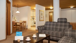 A cozy living room with a plaid sofa, a wooden coffee table, and a dining area with a table and chairs. - Chalet Abendrot apARTments by Interhome (Grindelwald)