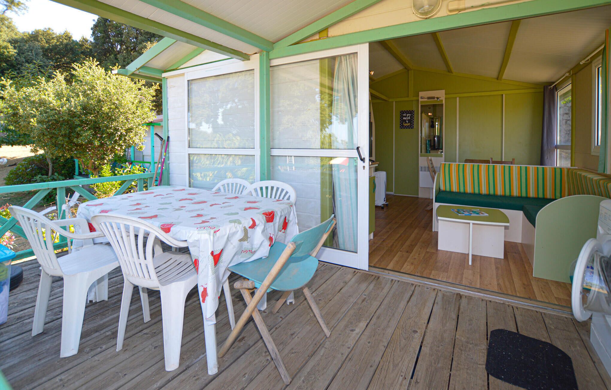 A covered patio with a table and chairs, a bench, and a door leading to an interior space.