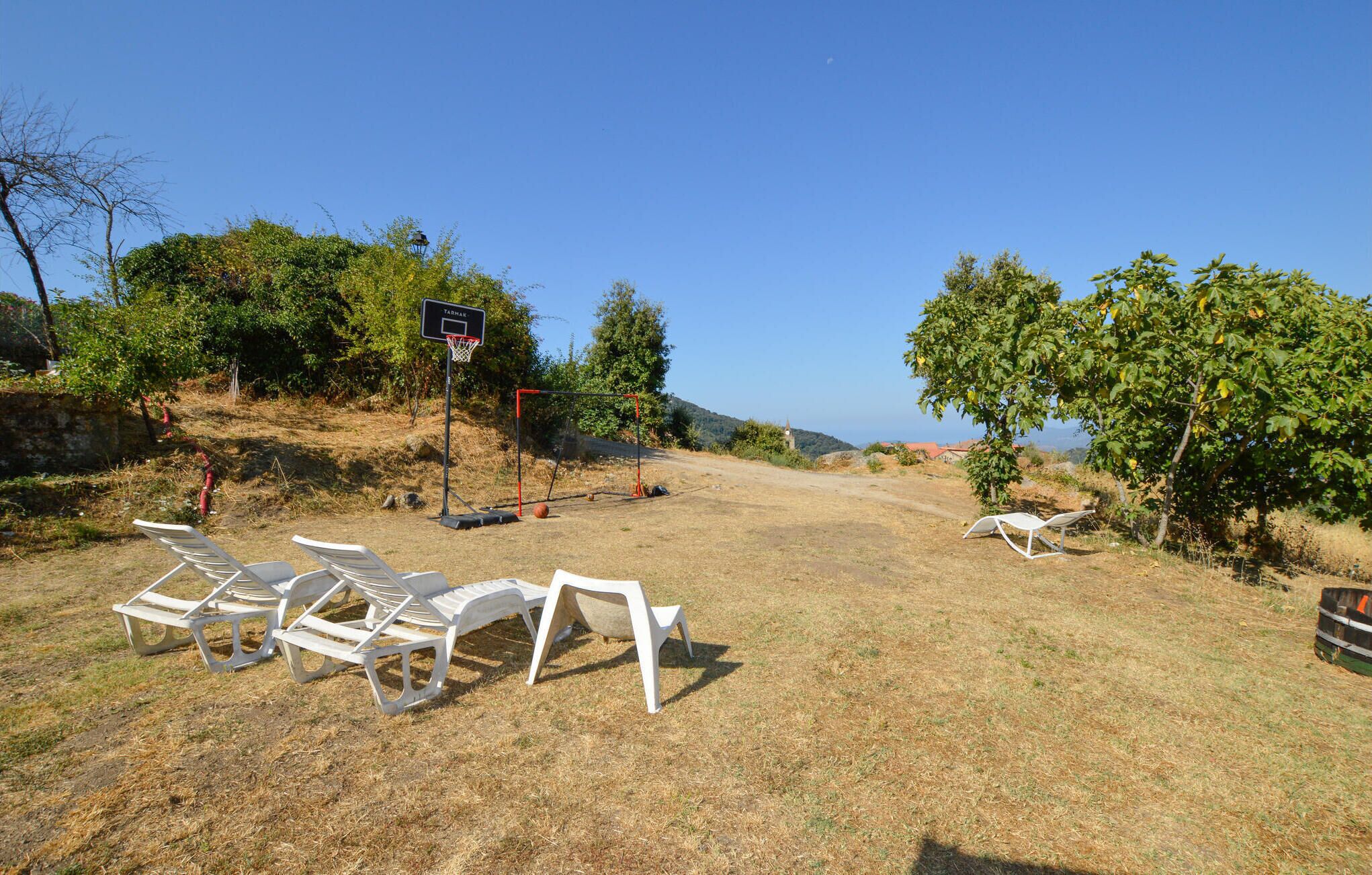 Ett soligt utomhusområde med en basketkorg, vita loungestolar och fri utsikt över havet.