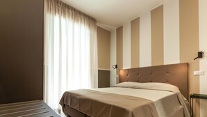 Ein Hotelzimmer mit Bett, Fenster mit Vorhängen, Wandleuchte und Nachttisch.