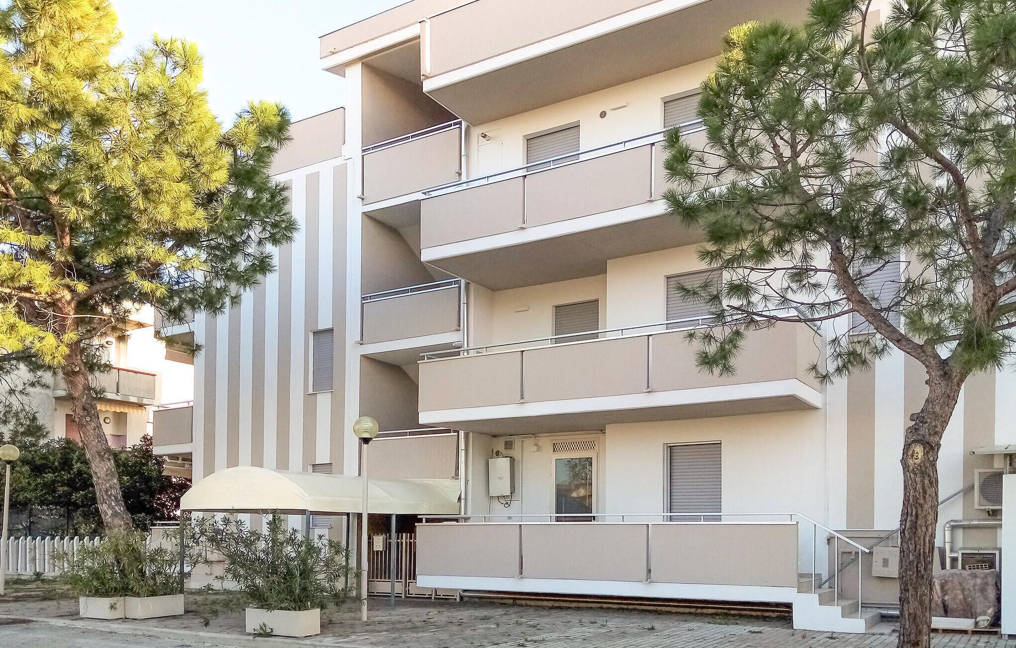 A multi-story residential building with balconies, a covered entrance, and surrounding trees.