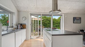 A modern kitchen with a central island, a built-in oven, and a large window overlooking a garden. - Beautiful home in Haderslev with sauna (Haderslev)