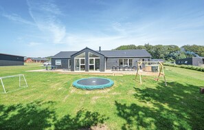 Une maison moderne dotée d’une grande porte vitrée, d’un trampoline et d’une balançoire dans le jardin.