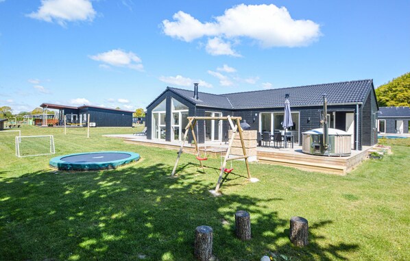 Une maison moderne dotée d’un patio, d’une balançoire, d’un trampoline et d’un jacuzzi.