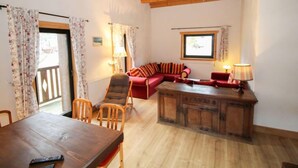 Ein gemütliches Wohnzimmer mit Holzboden, einem roten Sofa, einem Holztisch und einem Esstisch mit Stühlen.