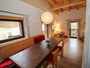 Ruokailutila, jossa on puinen pöytä ja tuolit, riippuvalaisin ja näkymä ikkunasta.