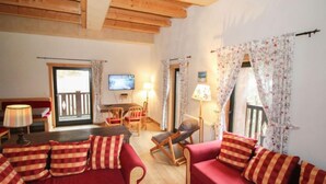 Ein gemütliches Wohnzimmer mit einer roten Sofagarnitur, einem Holzesstisch mit Stühlen, einem an der Wand montierten Fernseher und einem Balkon mit Blick.