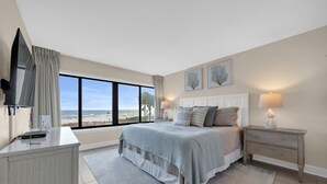 Ein Schlafzimmer mit großem Fenster, einem Bett, einem Nachttisch, einem Fernseher und einem Schreibtisch.