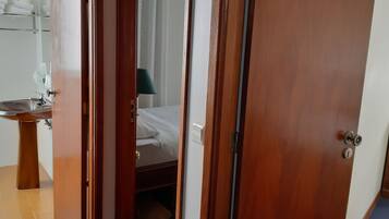 A wooden door with a keyhole, a mirror, a sink, and a bed with white linens.