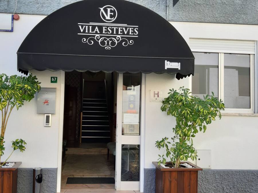 The entrance to Vila Esteves hotel with a black awning, a staircase leading inside, and two potted plants on either side.