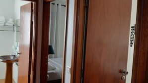 A hotel room with a wooden door, a bathroom with a sink and towel rack, and a bed with a white comforter. - Hotel Vila Esteves (Monção)