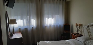 Un dormitorio con cama, una mesita de noche con lámpara, un televisor montado en la pared y una silla.